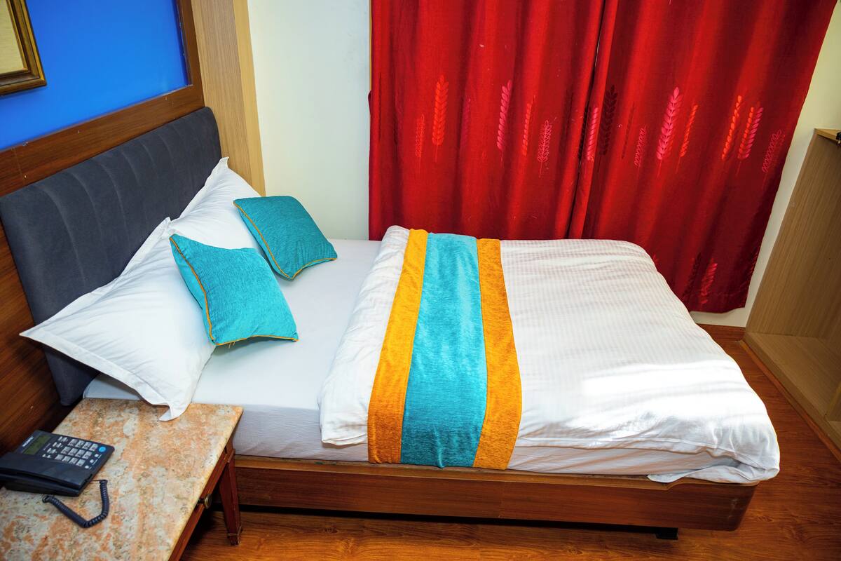 A neatly made bed with a striped blanket, two pillows, and a bedside table with a phone and a charger.