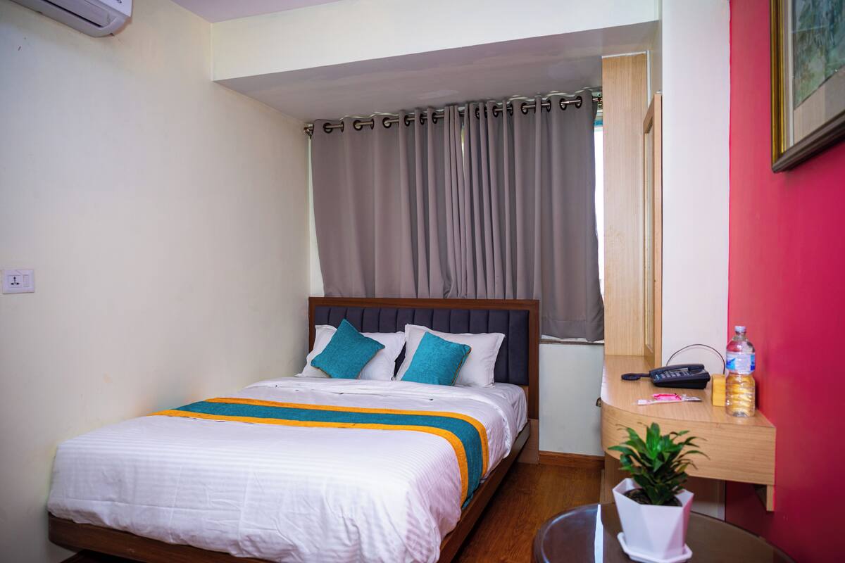 A neatly made bed with a striped bedspread, a bedside table with a plant, and a window with curtains.
