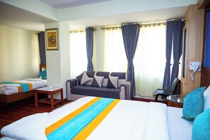A hotel room with a large bed, a sofa, a small table, and a chair. There is a window with curtains and a painting on the wall. - Hotel Sara Inn (Kathmandu)