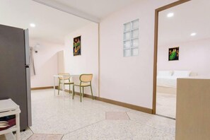 Quarto de hotel com cama, uma mesinha com cadeiras, geladeira e janela.