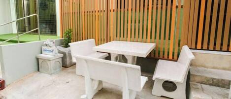 A small outdoor seating area with a table and benches, a small step leading up to a wooden fence, and a concrete floor.
