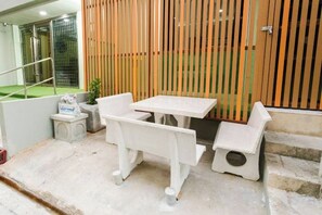 Uma pequena área externa com mesas e bancos, um degrau que leva a uma cerca de madeira, e piso de concreto.