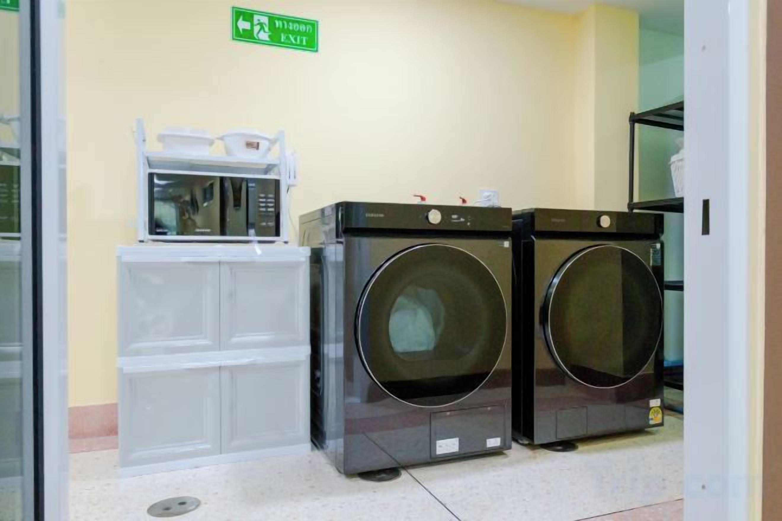 A laundry area with two front-loading washing machines and a dryer, a microwave, and a small cabinet.
