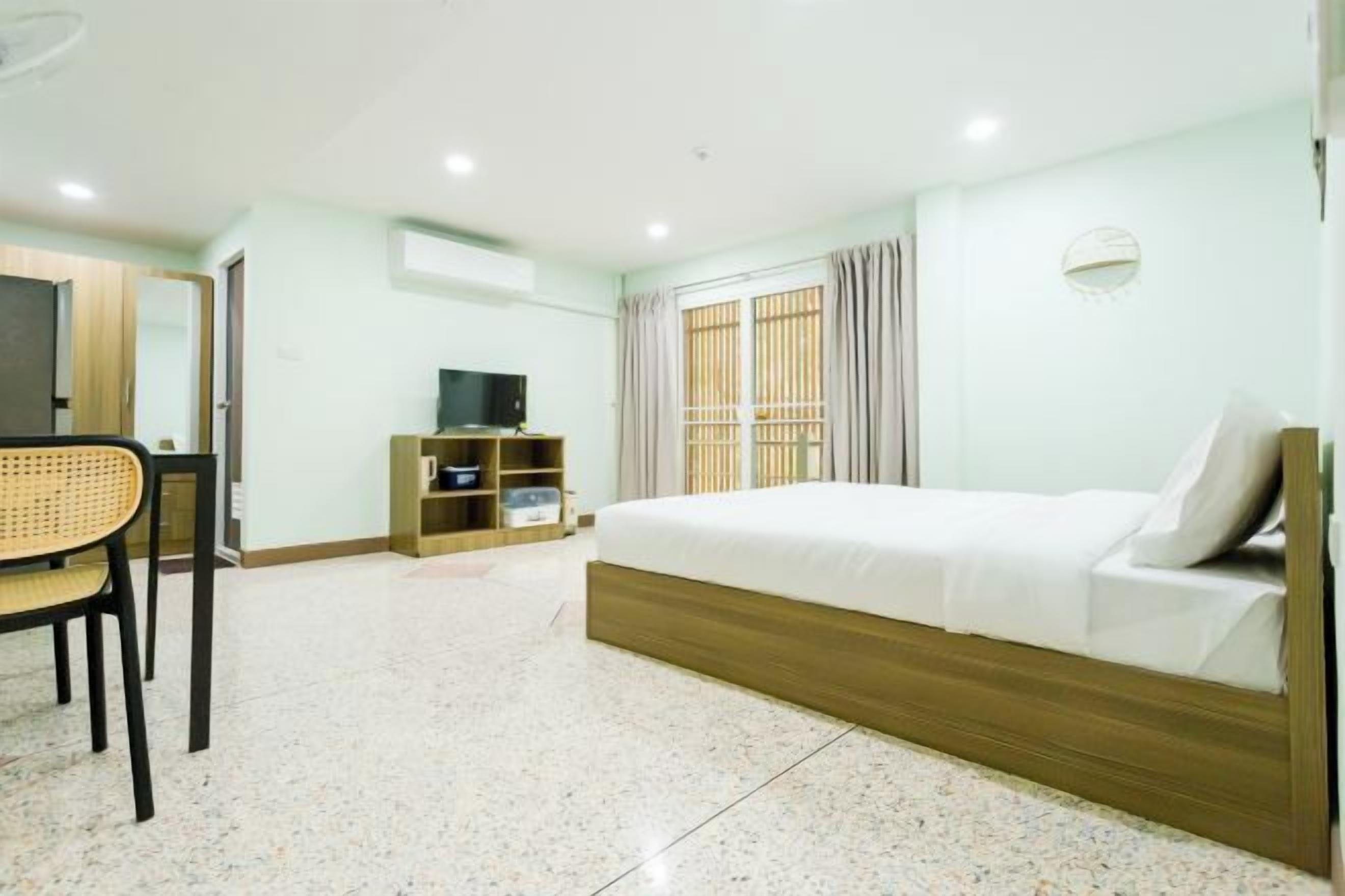A hotel room with a bed, a desk, a chair, a TV, and a wardrobe.