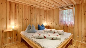 Habitación con paneles de madera, una cama, almohadas, una mesita de noche y una ventana con cortinas.