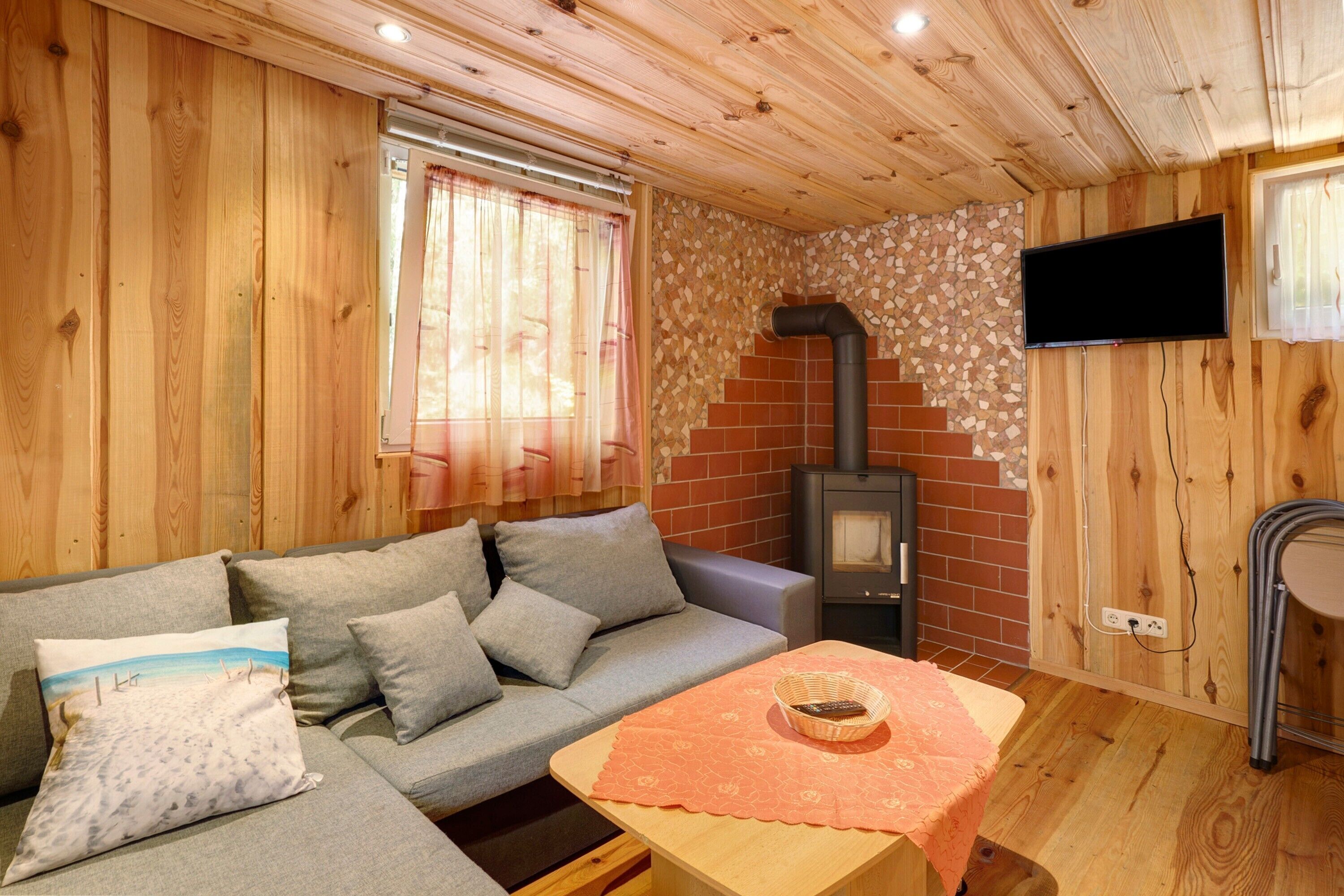 Ein gemütliches Blockhaus-Interieur mit einer Couch, einem Tisch mit Unterlage, einem an der Wand montierten Fernseher und einem Holzofen.