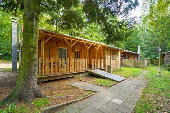 A wooden cabin with a porch, a ramp, and a stone pathway.
