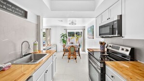 A modern kitchen with white cabinets, a stainless steel sink, and a wooden countertop. - Lower Villa Nature View-Heated Pool/Block to Sand (Fort Myers Beach)