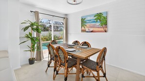 A dining area with a wooden table and chairs, a painting of a beach scene, and a potted plant. - Lower Villa Nature View-Heated Pool/Block to Sand (Fort Myers Beach)