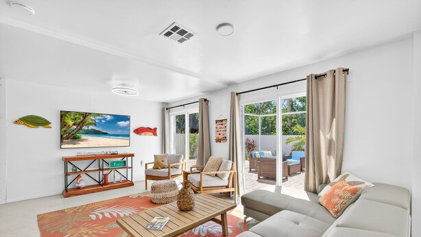 A modern living room with a sofa, coffee table, and chairs. There is a television mounted on the wall and a window with curtains. - Lower Villa Nature View-Heated Pool/Block to Sand (Fort Myers Beach)