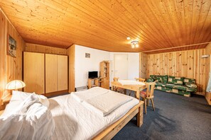 A wooden-paneled room with a bed, a desk, a television, and a green sofa.