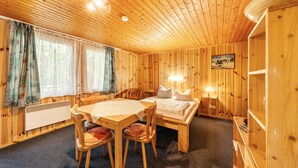 Interno di una baita in legno con tavolo, sedie, un letto e un termosifone.