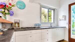 A kitchen with white cabinets, a gas stove, a sink, a window, and a clock on the wall. - 700m from the beach, garden, 4 adults 2 children (La Guérinière)