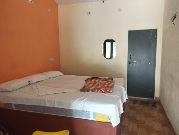 A single bed with a white mattress and a floral blanket, a small window, and a door.