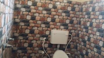 A small bathroom with a toilet, a white tank, and a tiled wall with a brick pattern.