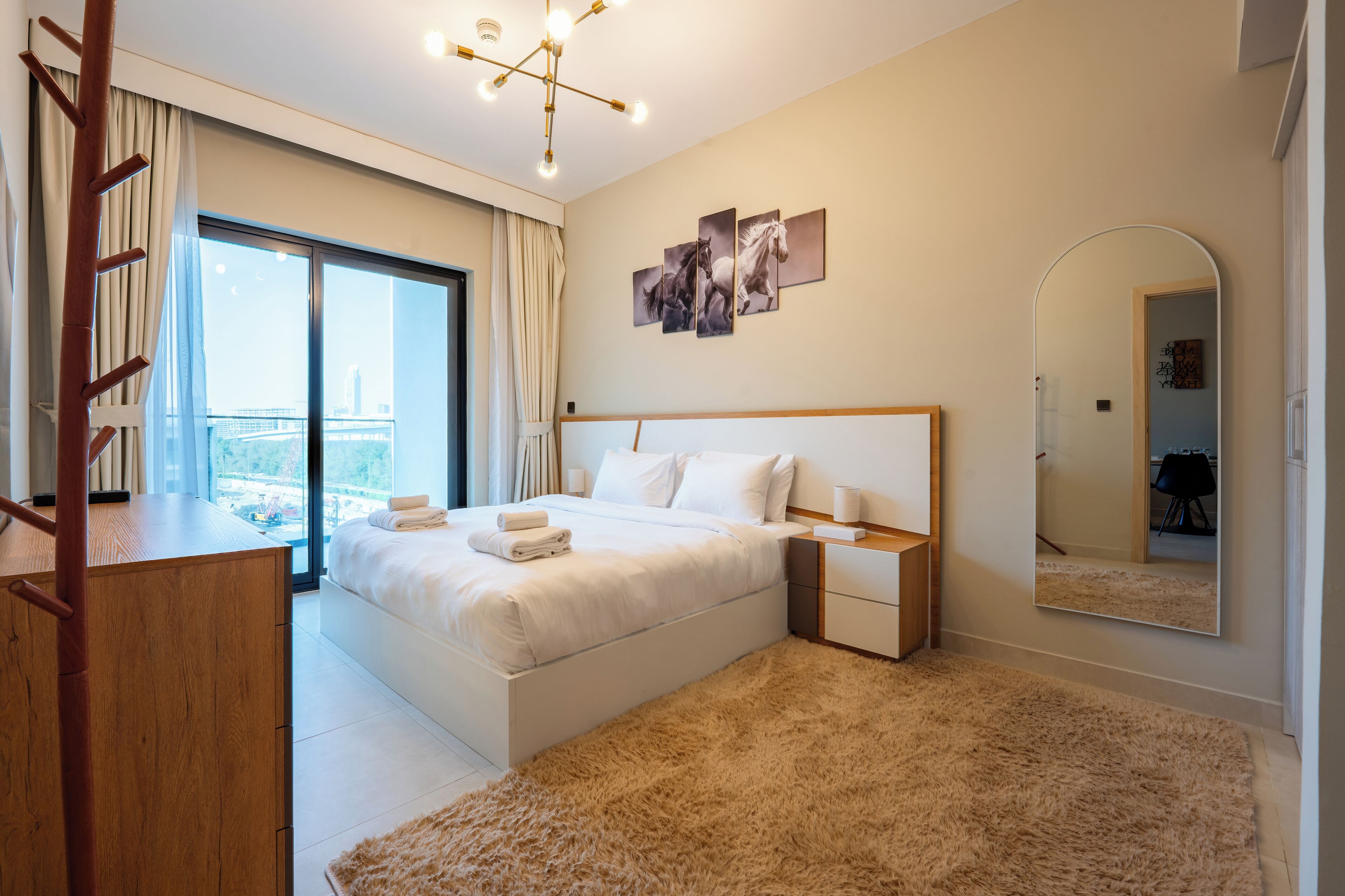 A modern hotel room with a large bed, a wooden desk, a fluffy rug, and a city view through the window.