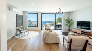 A modern living room with a large TV, comfortable seating, a round coffee table, and a view of the sea. - Villa Nero by LovelyStay (Funchal)
