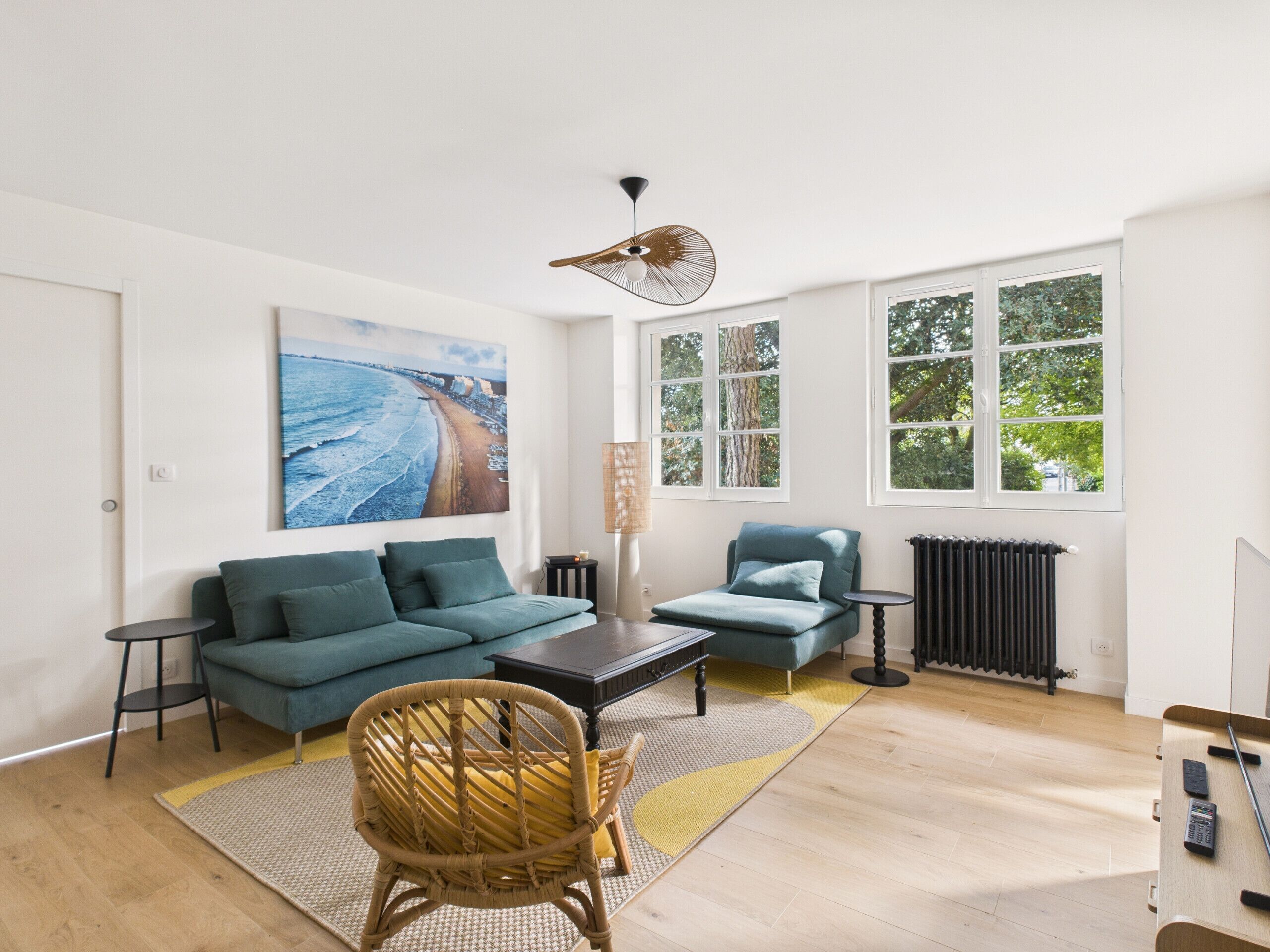 Ein modernes Wohnzimmer mit einer Couch, einem Sessel, einem Couchtisch und einem Bild von einem Strand.