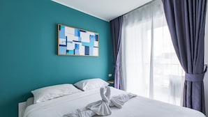 A hotel room with a teal wall, a bed with white linens, and a painting above the bed. - Pool View 1 Bed Apt T2-720 (Chalong)
