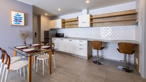 A modern kitchen with white cabinets, a black refrigerator, a microwave, and a dining area with a glass table and wooden chairs. - Pool View 1 Bed Apt T2-720 (Chalong)