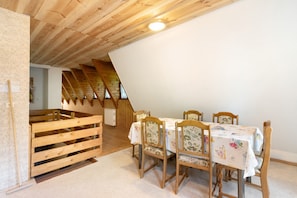 Un comedor con mesa y sillas de madera, techo inclinado y vista al espacio del ático.