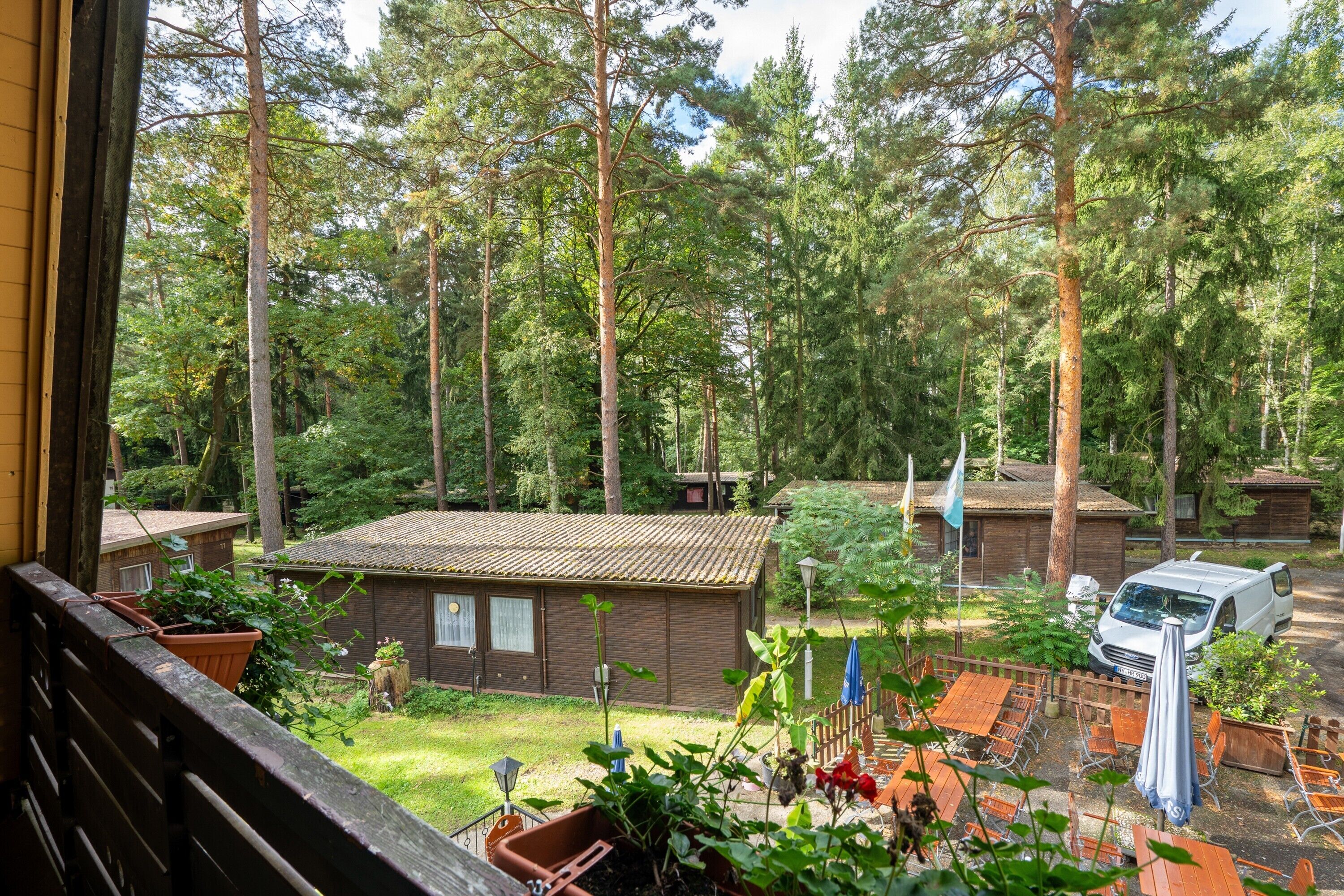 Eine Holzhütte mit Ziegeldach, umgeben von einem Wald, mit Sitzgelegenheit im Freien und einem geparkten Fahrzeug.