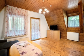 Habitación con paneles de madera, una cama, un televisor, una ventana con cortinas y un radiador.