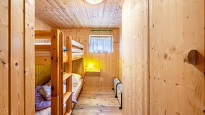 Un'accogliente baita in legno con letti a castello, una finestra con tende, un termosifone a parete e una luce a soffitto.