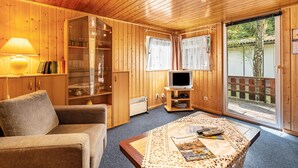 Una habitación acogedora con paredes de madera, un sofá, una mesa con revistas, un televisor y una ventana con cortinas.