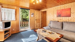 Una habitación con paneles de madera, un sofá, un televisor, una mesa con posavasos y una puerta que da al exterior.