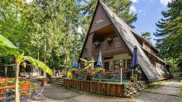 A wooden cabin with a sloped roof, surrounded by trees, and featuring outdoor seating with umbrellas.