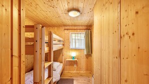 Una cabaña de madera con literas, una mesita con lámpara y una ventana con cortinas.