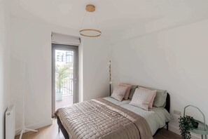 Une chambre à coucher avec un lit, une table de chevet, un luminaire suspendu et une vue sur l’extérieur, visible à travers une porte.