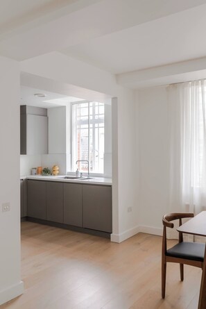 Une cuisine moderne avec des meubles gris, un évier et une fenêtre agrémentée de rideaux blancs.