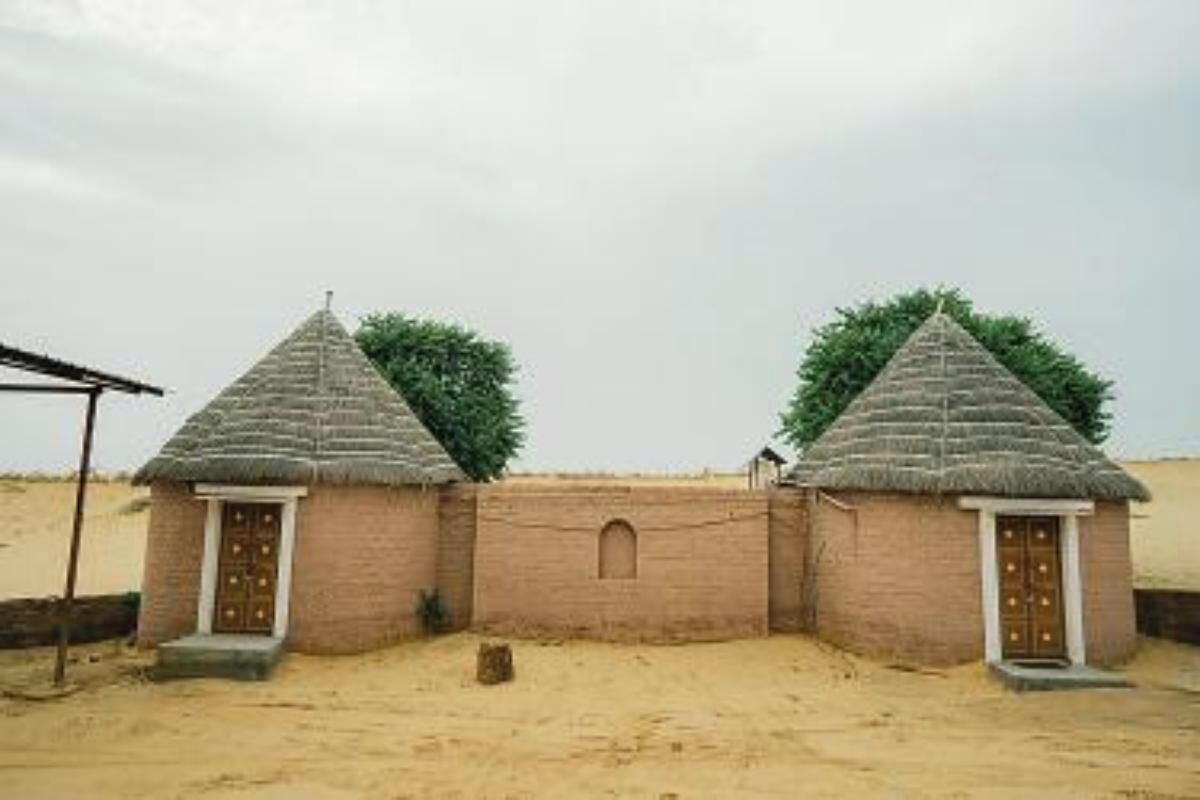 Two thatched-roof huts with wooden doors, set against a sandy background.