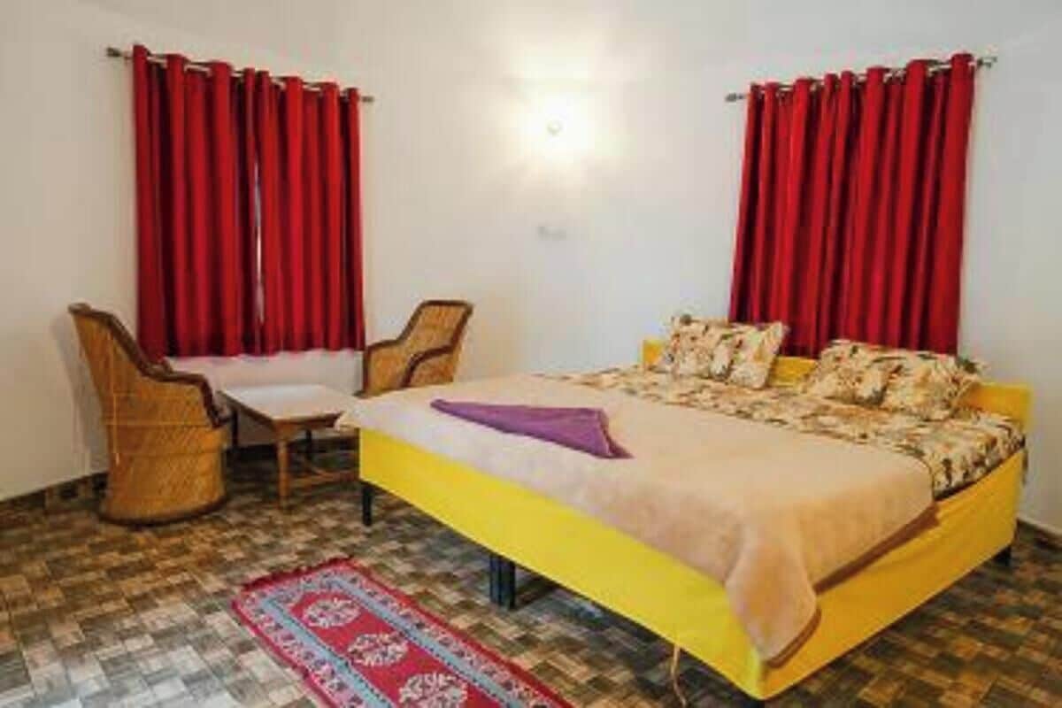 A room with a bed, two chairs, red curtains, and a patterned rug.