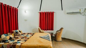 A room with a bed, a chair, a small table, and a red curtain. - Bhati Desert Camp Raisar Bikaner (Bikaner)