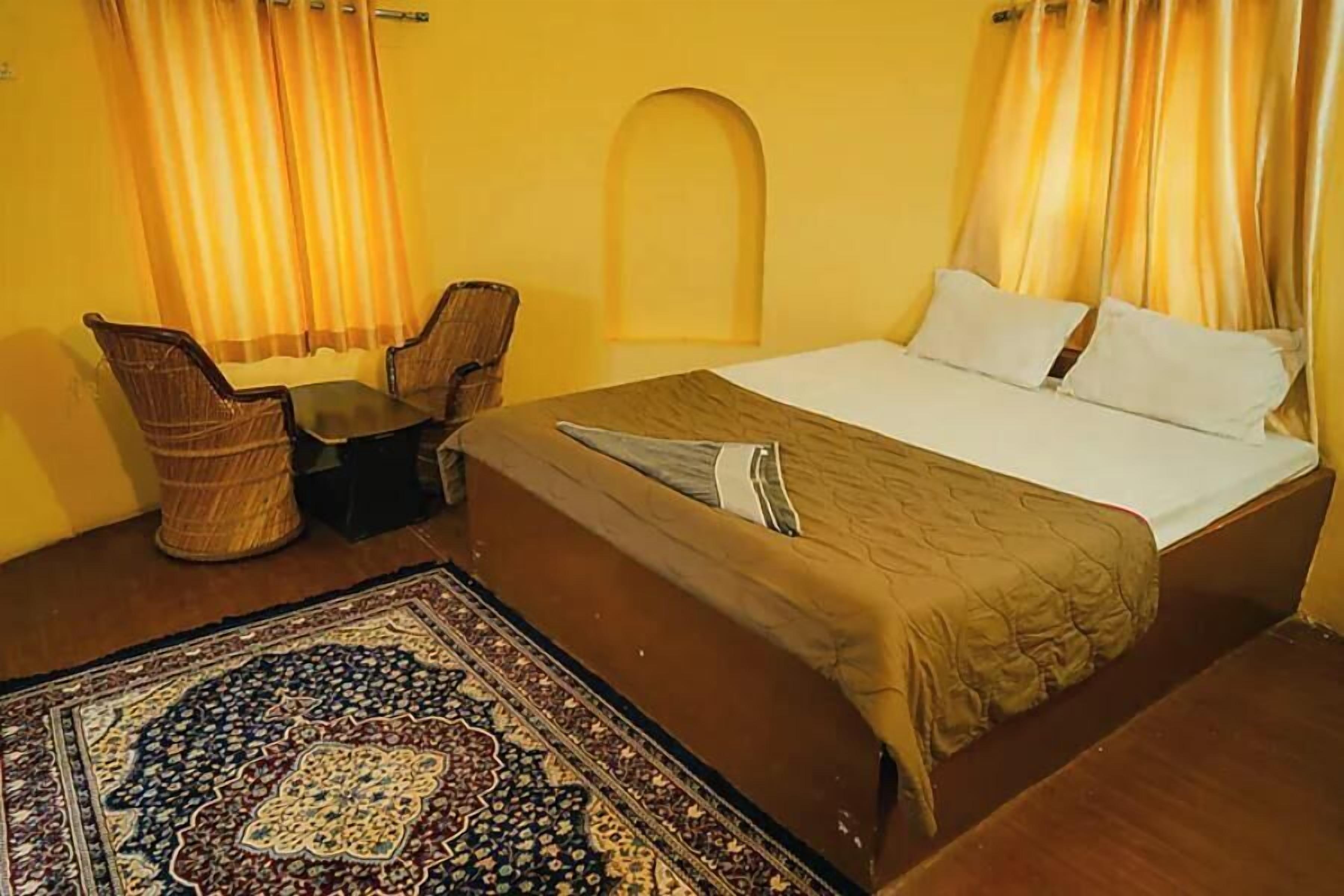 A hotel room with a bed, two chairs, a small table, and a patterned rug.
