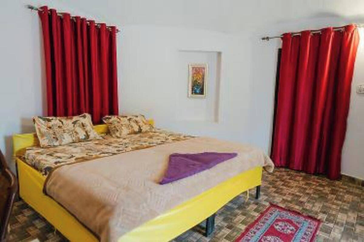 A bed with a patterned bedspread, a yellow headboard, and red curtains.