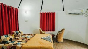 A room with a bed, a chair, a red curtain, and a wall-mounted air conditioning unit. - Bhati Desert Camp Raisar Bikaner (Bikaner)