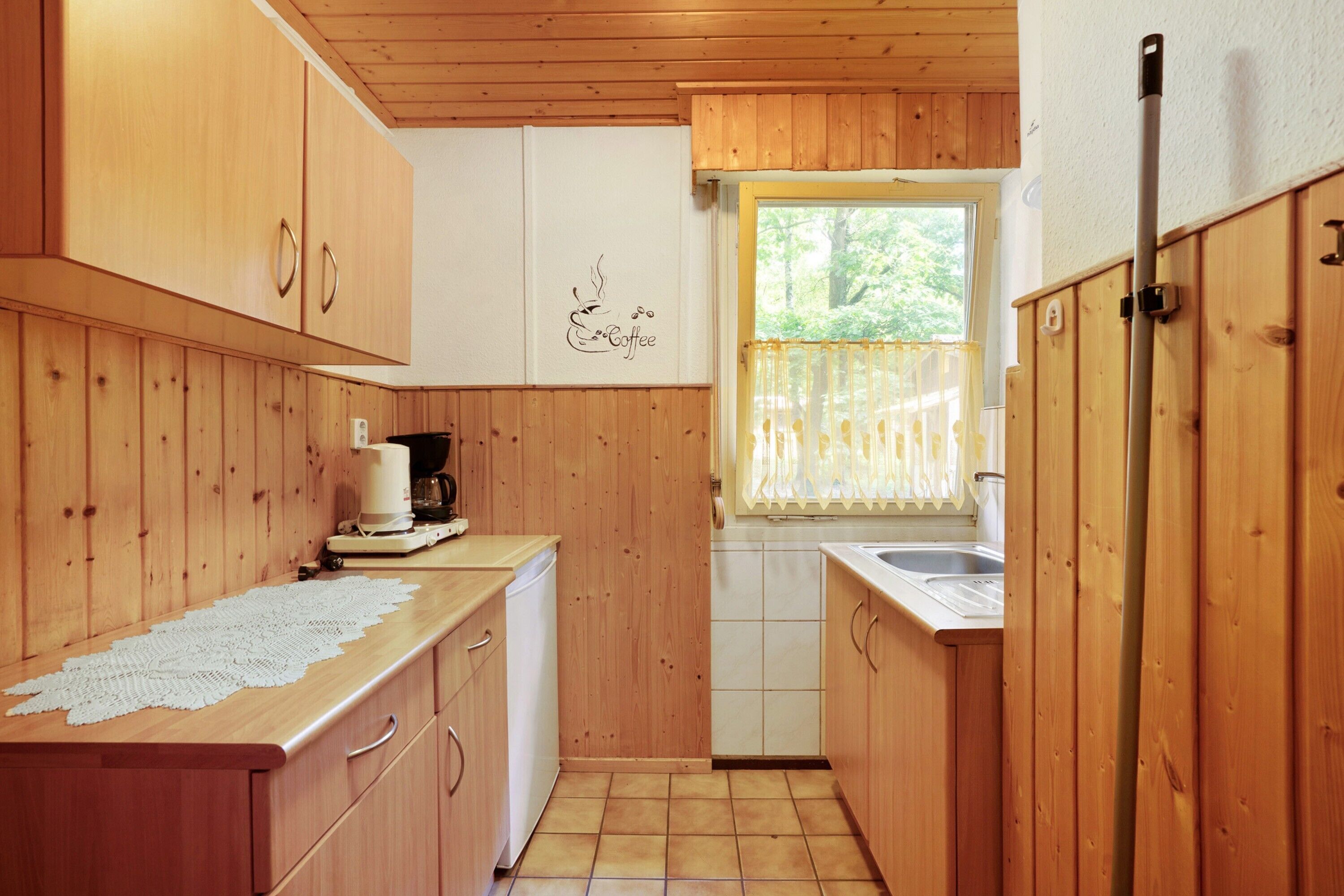 A compact kitchen with wooden cabinets, a coffee machine, and a window with a view of greenery.