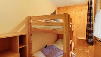 A bunk bed with a pillow and a blanket, wooden walls, a shelf, and a window with a curtain.