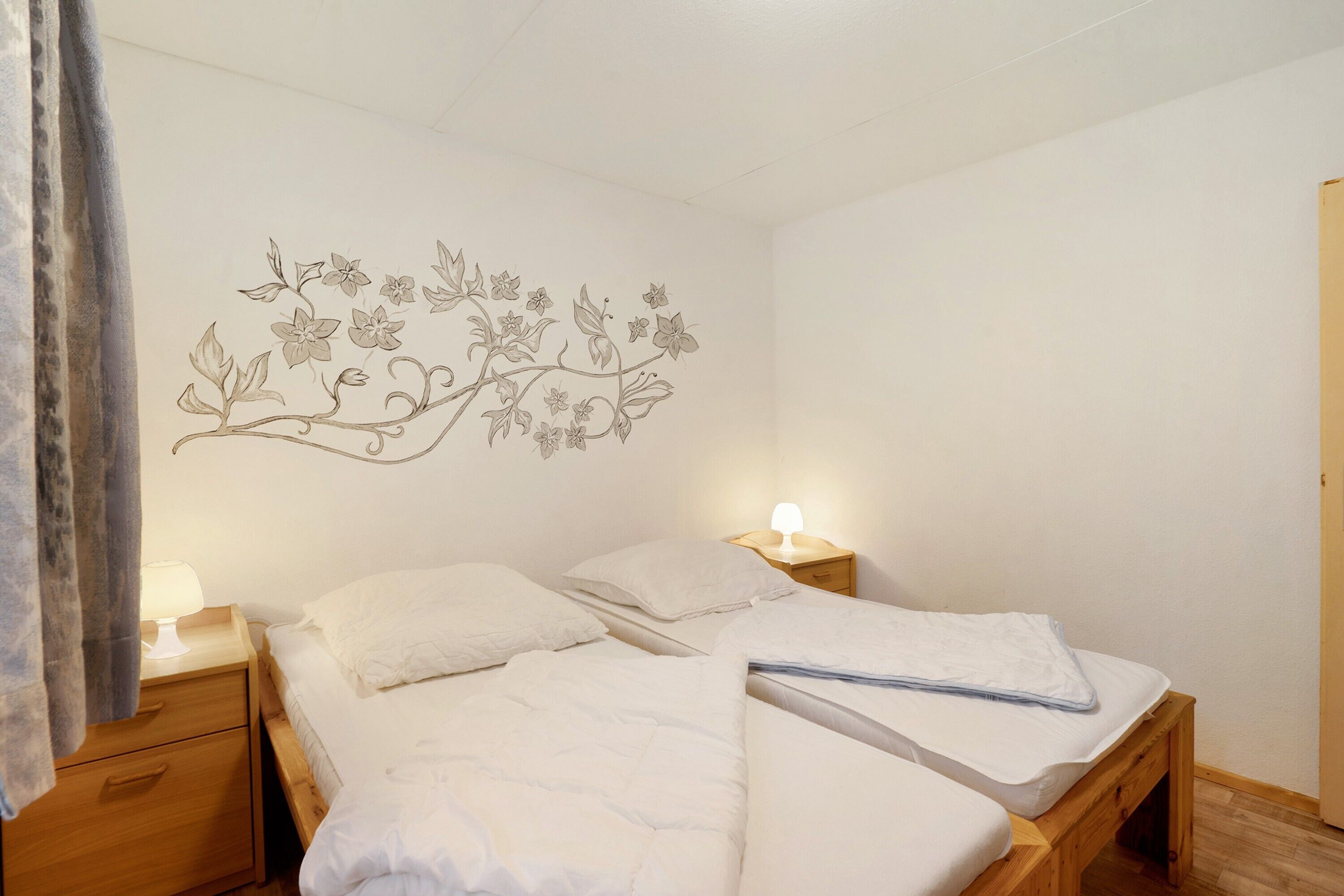 A bedroom with a bed, two bedside tables, a wall mural, and a door.
