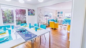 A modern living room with a dining area, featuring a large table, blue and yellow chairs, and a sofa. - 3 Coastal View Houses in 1: Seaview 3BD+ Seasong 2BD* + Selah 4BD (Crescent City)