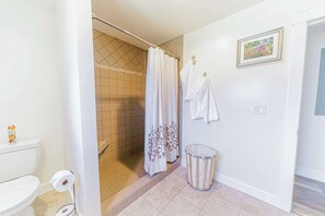 Een badkamer met een douche, toilet en een prullenbak.