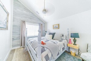 Een slaapkamer met een bed, nachtkastje, lamp en een raam met gordijnen.