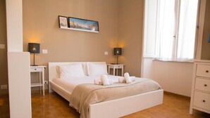 Un dormitorio con una cama, dos mesitas de noche, un tocador y un armario, además de una ventana con cortinas.