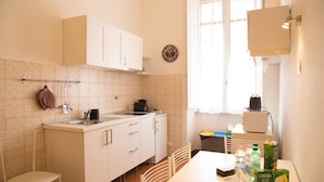 Una cocina con armarios blancos, un lavamanos y una ventana. Hay sillas, una mesa y algunos alimentos sobre la mesa.