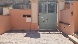 Una entrada cerrada con un portón metálico, un pequeño ventanal con ventilación y un pavimento de baldosas.