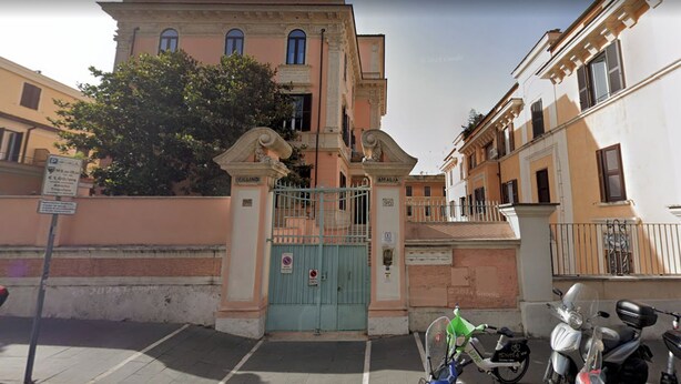 Vista de la calle con un acceso porticado, scooters estacionados y un edificio de fachada clásica.